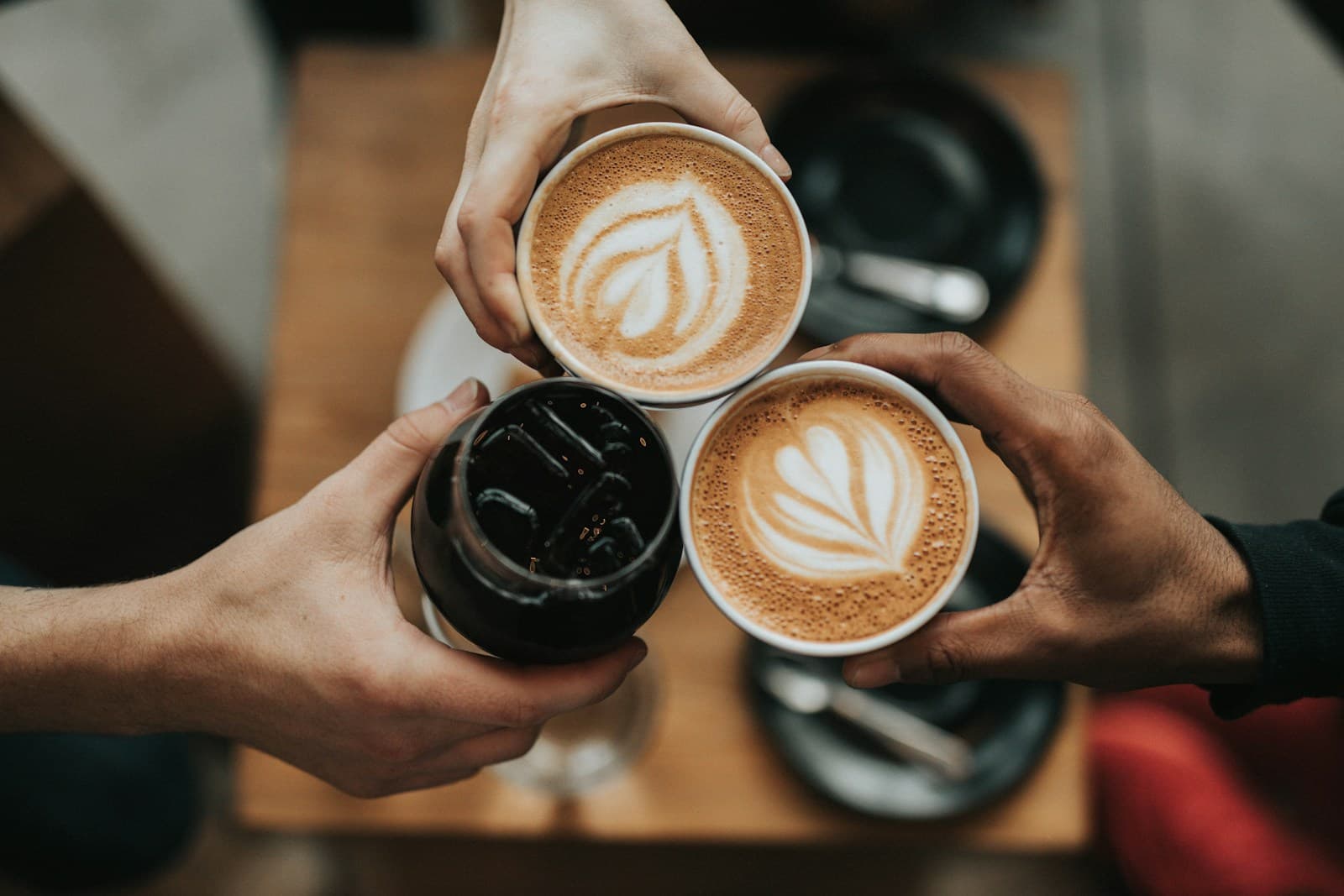 Friends holding lattes and iced coffee together; coffee-themed photography